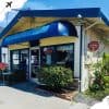 Gulf Breeze Cafe exterior with blue awning, open sign, surrounding greenery, and clear sky in a charming coastal town setting. Ideal for travel destinations and sightseeing.