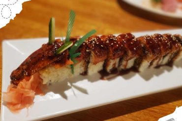 Savory sushi roll with eel, rice, and toppings drizzled in eel sauce served on a white rectangular plate. Perfect for sushi lovers seeking authentic Japanese cuisine.