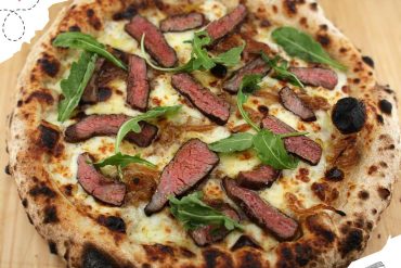 Juicy grilled steak on a gourmet pizza with arugula and caramelized onions, crispy crust, and melted cheese, perfect for food lovers and pizza enthusiasts.