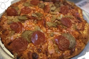 Pizza with pepperoni, sausage, and ham on a metal tray, showcasing delicious Italian food and travel cuisine, perfect for food tourism and international culinary adventures.