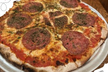 Savory pepperoni pizza with herbs on a metal tray, showcasing a crispy crust and melted cheese, perfect for exploring culinary destinations and delicious food experiences.