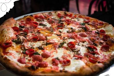 Freshly baked pepperoni pizza with melted cheese, mushrooms, and herbs on a rustic crust served hot at a cozy restaurant. Perfect comfort food for pizza lovers, ideal for travel and food tourism.