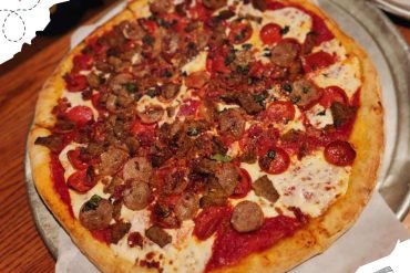 Vegetarian and meat pizza with pepperoni, sausage, and fresh herbs on a thin crust served on a metal tray.