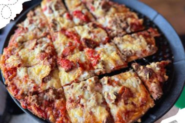 Savory meat pizza with melted cheese, toppings, and crispy crust served on a black pizza tray, perfect for a food tour or travel experience at a travel destination.
