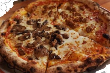 Pizza with mushrooms and sausage on a wooden table, delicious Italian pizza, cheese topping, casual dining, go to destinations, food and travel, culinary experience, pizza restaurant, gourmet pizza, travel dining experience.