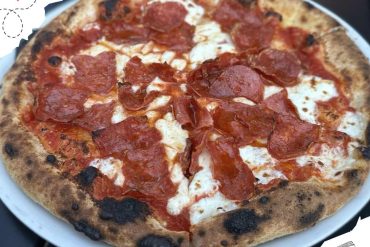 Thin-crust pepperoni pizza with melted cheese on a white plate, showcasing classic Italian-style pizza ready for travel or dining.