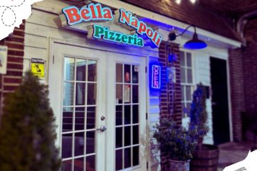 Bella Napoli Pizzeria exterior at night with neon "Open" sign, cozy outdoor lighting, and welcoming entrance, emphasizing authentic Italian pizza dining experience.