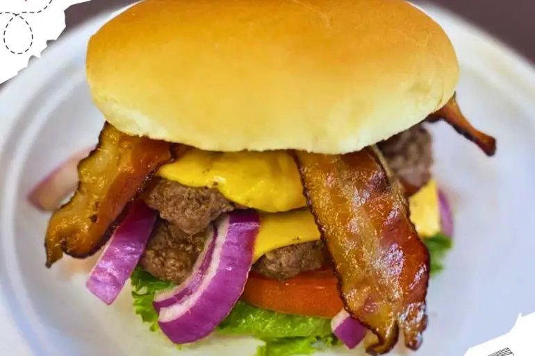 Cheeseburger with bacon and raw purple onions on a white plate.
