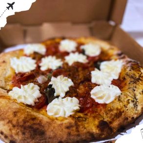 A small pizza in a box with pepperoni and dollops of cream.