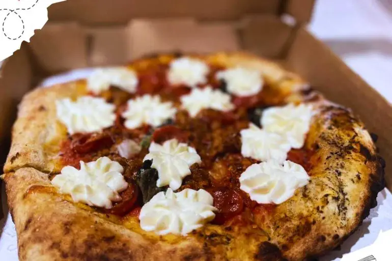 A small pizza in a box with pepperoni and dollops of cream.