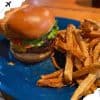Beef burger with lettuce, tomato, and toasted bun served with crispy French fries on a blue plate. Perfect comfort food for travel and leisure.