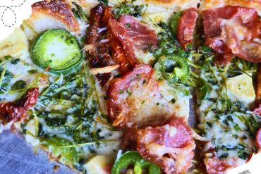 A close up of a slice of pizza with jalepenos and pepperoni.