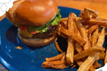 Beef burger with lettuce, tomato, and toasted bun served with crispy French fries on a blue plate. Perfect comfort food for travel and leisure.