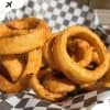 Crispy golden onion rings on checkered paper in basket, delicious fried appetizer, perfect for travel snacks or casual dining, popular comfort food for food lovers, close-up shot.