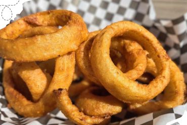 Crispy golden onion rings on checkered paper in basket, delicious fried appetizer, perfect for travel snacks or casual dining, popular comfort food for food lovers, close-up shot.