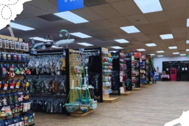Clothing and toy store aisle with baby items and accessories for travel and essentials for infants and toddlers, shelves filled with colorful baby products, in an indoor retail environment.