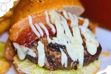 Juicy bacon cheeseburger with melted cheese, fresh lettuce, tomato, and creamy sauce on a toasted bun, served as a delicious fast food meal. Perfect for burger lovers.