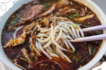 Spicy Asian noodle soup with beef and herbs in a bowl, close-up image.
