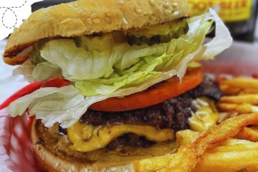 Fresh classic cheeseburger with lettuce, tomato, pickles, melted cheese, and crispy fries, showcasing delicious American fast food options for travelers seeking tasty destinations.