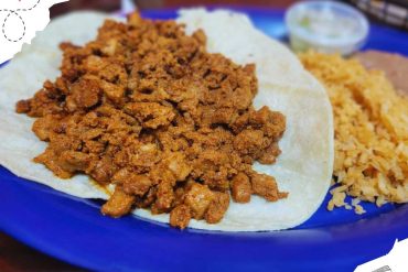 Ground beef taco filling on a soft tortilla with rice on a blue plate, authentic Mexican cuisine.
