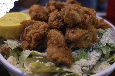 Crispy fried chicken tenders on a bed of fresh lettuce with grated cheese and lemon wedge, served with dipping sauce, in a white bowl, perfect for travel food and international cuisine experiences.