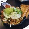Savory Mexican carne asada fries bowl topped with lettuce, guacamole, fried egg, and crispy toasted bread slices, served with spicy salsa on the side, perfect for food travel experiences.