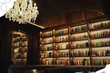 Vintage library with tall wooden bookshelves filled with colorful books, illuminated warm lighting, elegant chandeliers, cozy reading and dining space, perfect for travel-inspired destinations and cultural exploration.