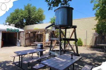 Vibrant outdoor dining area at Go To Destinations with picnic tables, shaded by trees, featuring a water tower and casual food setup in a relaxed backyard setting.