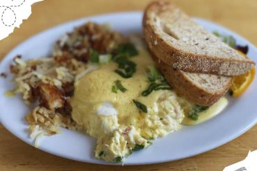 Scrambled eggs with green onions, crispy breakfast potatoes, and toasted whole wheat bread on a white plate, served as a hearty breakfast meal.