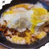 Savory breakfast dish with melted cheese, seasoned meats, and fried egg on top in a black skillet, popular comfort food, delicious brunch option, hearty meal, served hot.