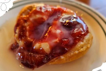 Sweet breakfast biscuit topped with rich berry jam and melted butter, served on a white plate for a delicious travel-inspired meal at Go To Destinations.