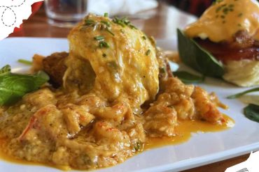 Savory seafood dish featuring a lobster tail coated in rich, creamy sauce garnished with fresh herbs, served with lettuce leaves on a white plate. Perfect for food lovers exploring global cuisine.