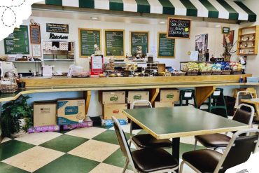 Green and white checkered flooring inside a casual cafe or convenience store with shelves of snacks, menu boards, and seating area, ideal for travel destination and dining experiences.