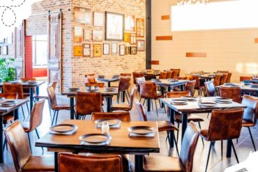 Cozy modern restaurant interior with rustic brick walls, wooden tables and leather chairs, perfect for dining and travel destinations, featuring warm lighting and framed artwork.