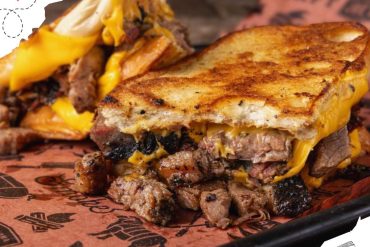 Savory grilled cheese sandwiches with melted cheddar and tender beef, served with crispy fries on a black tray.
