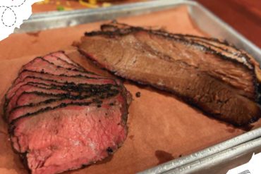 Succulent medium-rare grilled steak with charred grill marks on top, sliced and served on a metal tray with parchment paper, showcasing delicious beef for meat lovers and barbecue enthusiasts.