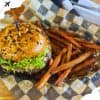Crispy sweet potato fries with gourmet burger topped with lettuce and chocolate chips, served in a checkered paper basket at a modern cafe.