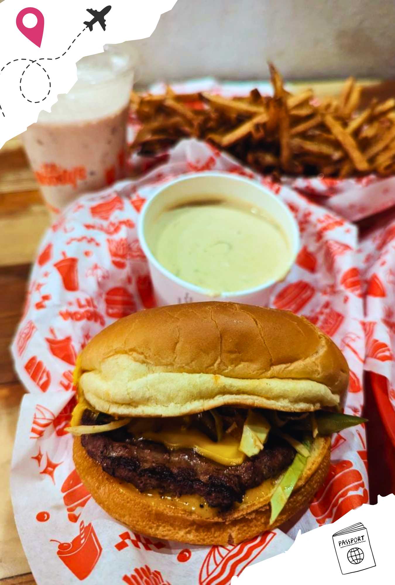 A burger with a cup of dipping sauce and French fries behind it.