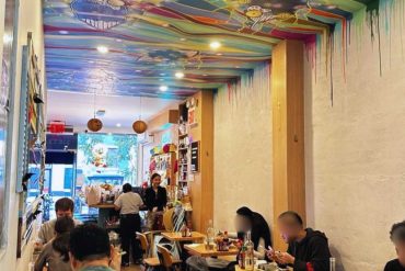 Colorful artistic restaurant interior with vibrant ceiling art, casual dining atmosphere, and diverse group of patrons enjoying meals, perfect for travel and culinary exploration.
