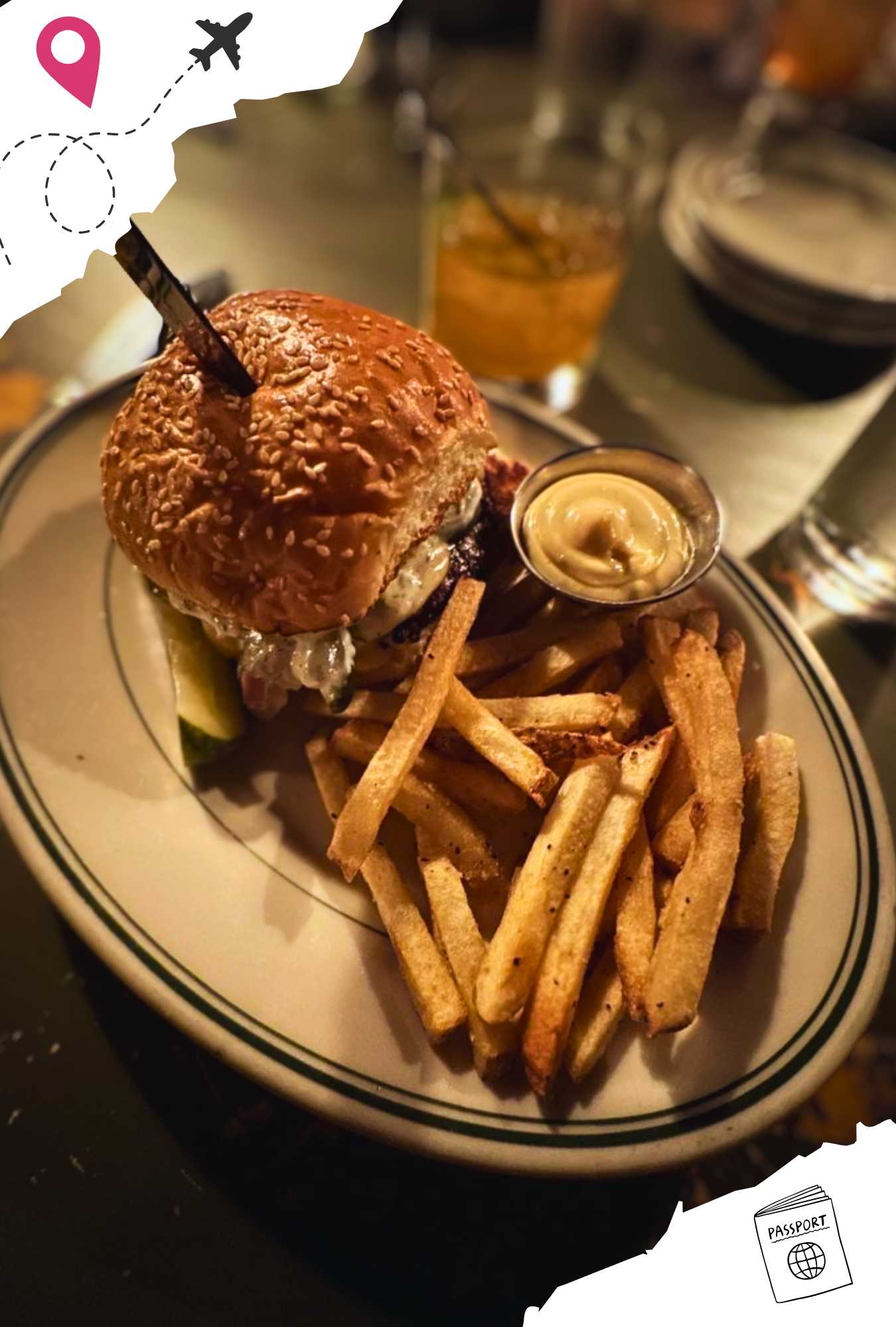 A burger with a knife stuck in the top with a side of French fries and a cup of dipping sauce.