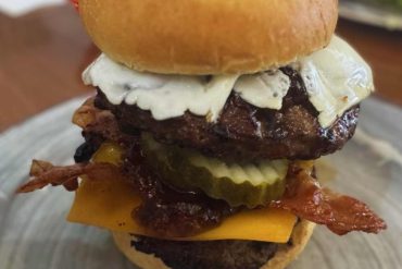 Fresh gourmet burger with bacon, cheese, pickles, and creamy sauce on a toasted bun, served on a rustic plate. Perfect for travel destinations to enjoy delicious comfort food abroad.