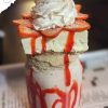 Sweet strawberry ice cream sundae with whipped cream and strawberry slices, drizzled with strawberry syrup in a tall glass. Perfect for dessert and travel destination snacks.