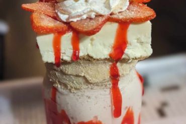 Sweet strawberry ice cream sundae with whipped cream and strawberry slices, drizzled with strawberry syrup in a tall glass. Perfect for dessert and travel destination snacks.