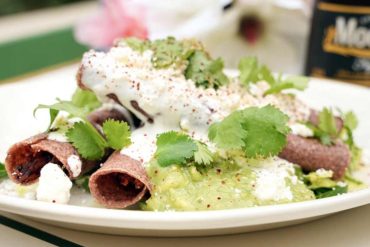 Crispy beef tacos with fresh cilantro and creamy sauce, Mexican street food, outdoor dining, vibrant flavors, popular travel destination food experience.