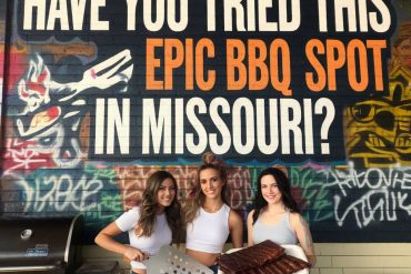 Succulent grilled ribs at an outdoor barbecue spot in Missouri with three smiling women standing in front of colorful graffiti wall.