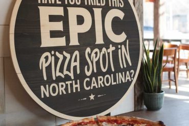 Delicious pizza served at a North Carolina pizzeria with a prominent chalkboard-style sign inviting diners to try an epic pizza spot. Perfect for restaurant and food lover SEO.