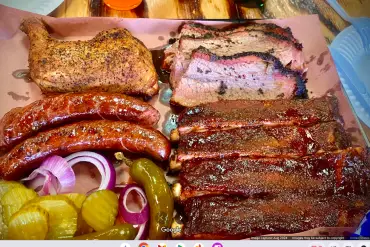 Smoked BBQ ribs, grilled chicken, sausages, pickles, and onions served on parchment paper. Delicious southern-style barbecue with savory flavors and smoky aroma. Perfect for meat lovers and barbecue enthusiasts.