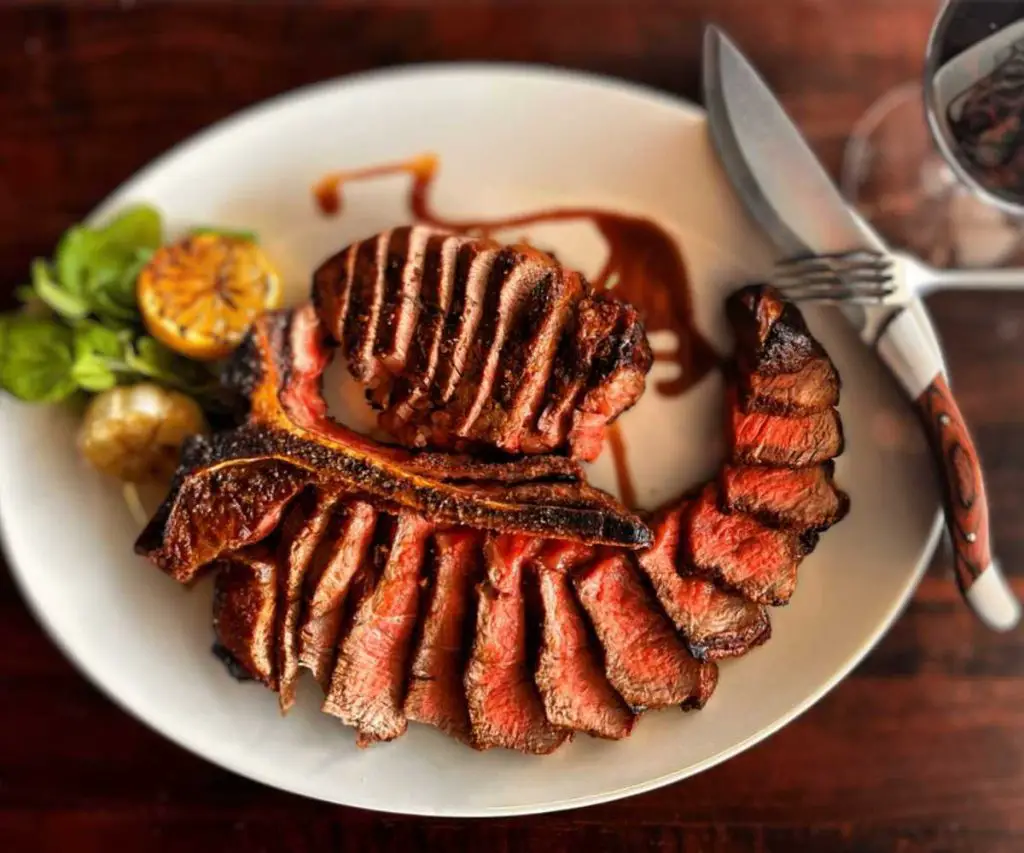 Juicy grilled steak served with fresh herbs, citrus, and drizzled with sauce, on a white plate perfect for savoring delicious American BBQ cuisine.