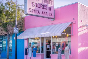 Pink storefront of a thrift store with mannequins displaying vintage clothes, sign reading "Best Thrift Stores in Santa Ana, CA", colorful exterior, highlighting Santa Ana shopping destinations.