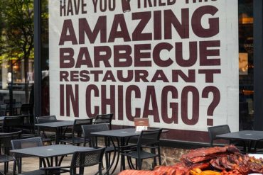 Succulent barbecued meats served outdoors at a Chicago barbecue restaurant with promotional signage in the background.